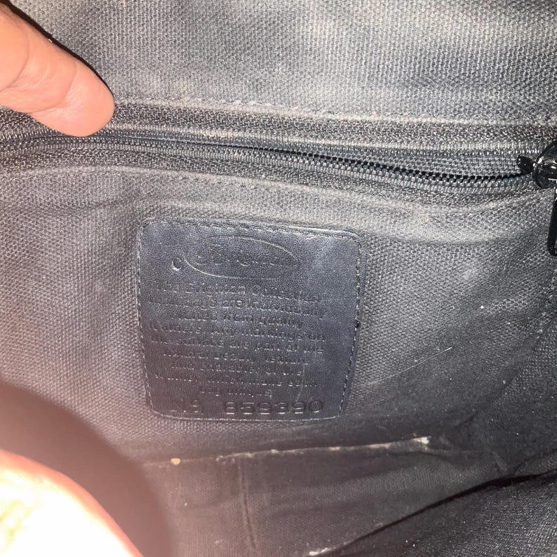 May include: Interior view of a black fabric bag with a zipper and a leather tag. The tag has text and the number 1953390. The bag's interior is dark and textured.