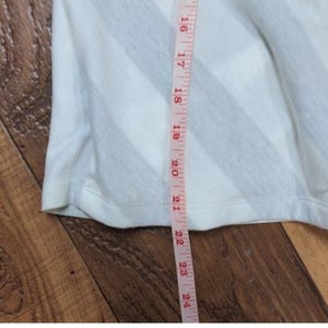 May include: White and gray striped fabric with a measuring tape alongside it. The tape shows measurements from 16 to 24 inches. The fabric appears to be part of a garment, possibly a shirt or dress.