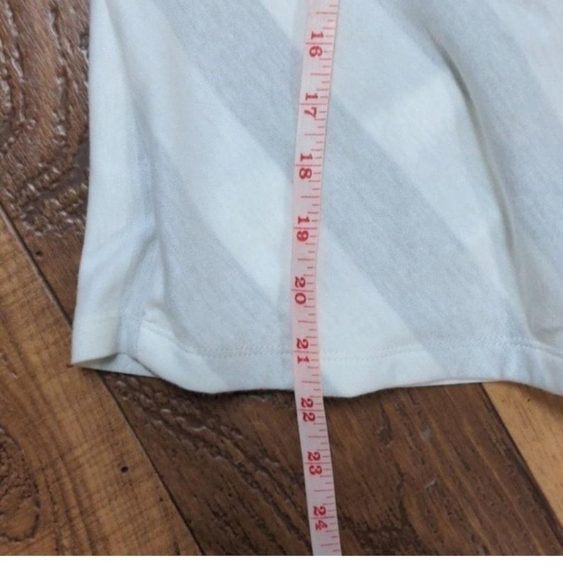 May include: White and gray striped fabric with a measuring tape alongside it. The tape shows measurements from 16 to 24 inches. The fabric appears to be part of a garment, possibly a shirt or dress.
