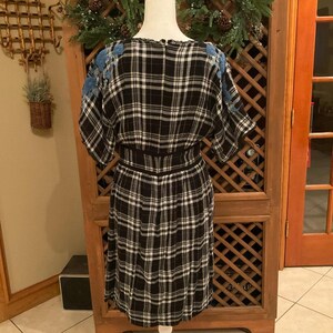 May include: A black and white plaid dress with blue floral embroidery on the shoulders. The dress has a fitted waist and a knee-length skirt. The dress is displayed on a mannequin.