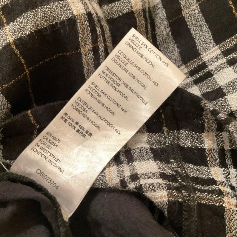 May include: Close-up of a fabric with a black and white plaid pattern. A white tag is visible, listing fabric composition and care instructions. The tag also includes the brand's RN number, CA number, and address in London.