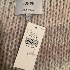May include: Close-up of a chunky knit sweater in shades of cream, pink, and gray. The sweater has a tag that reads "N&Uuml;MPH" and "MAKE AN ENTRANCE". A size "L" tag is attached. The sweater's texture is visible.