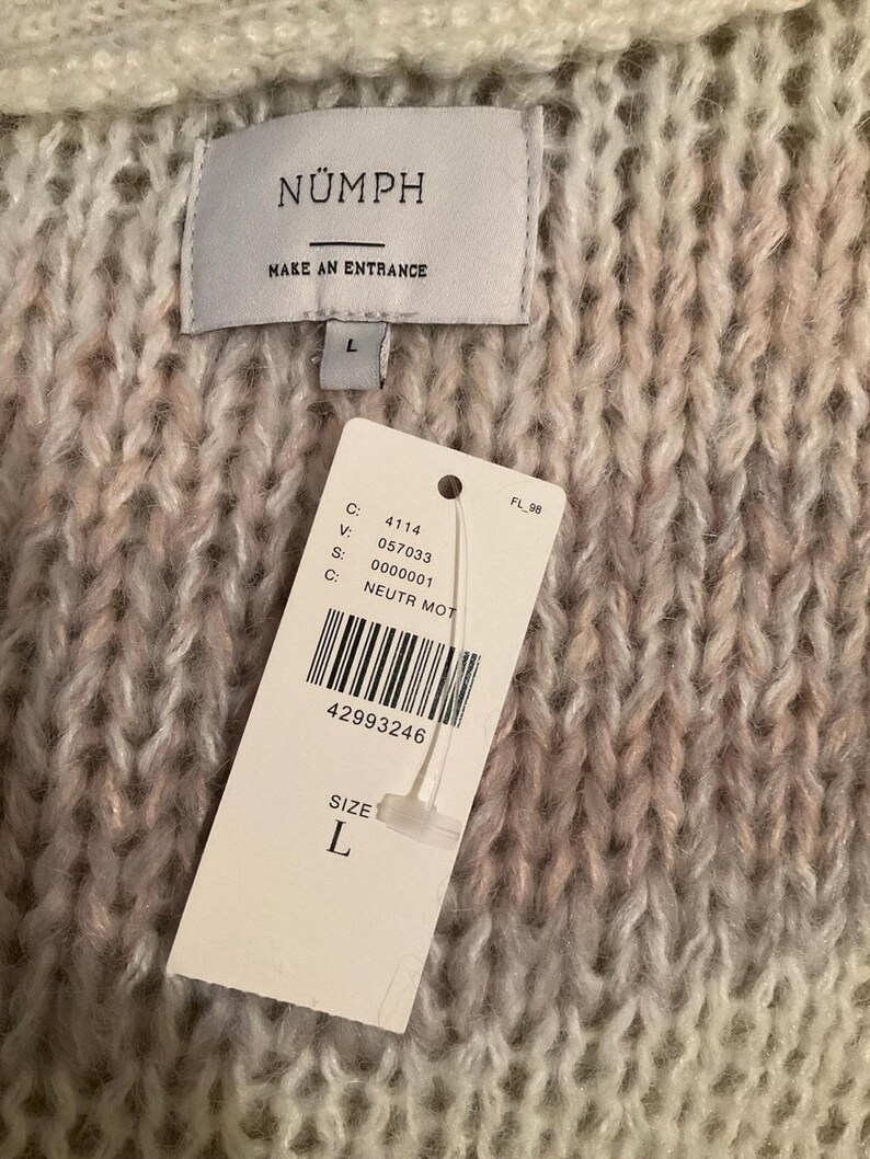 May include: Close-up of a chunky knit sweater in shades of cream, pink, and gray. The sweater has a tag that reads "N&Uuml;MPH" and "MAKE AN ENTRANCE". A size "L" tag is attached. The sweater's texture is visible.