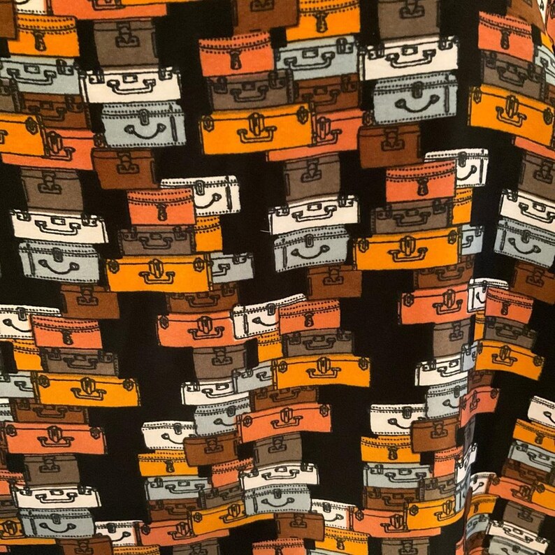 Puede incluir: Tela negra con un patr&oacute;n repetido de maletas vintage en varios colores, incluyendo naranja, marr&oacute;n, gris y blanco. Las maletas est&aacute;n apiladas y dispuestas en un patr&oacute;n aparentemente aleatorio, creando un dise&ntilde;o tem&aacute;tico de viajes.