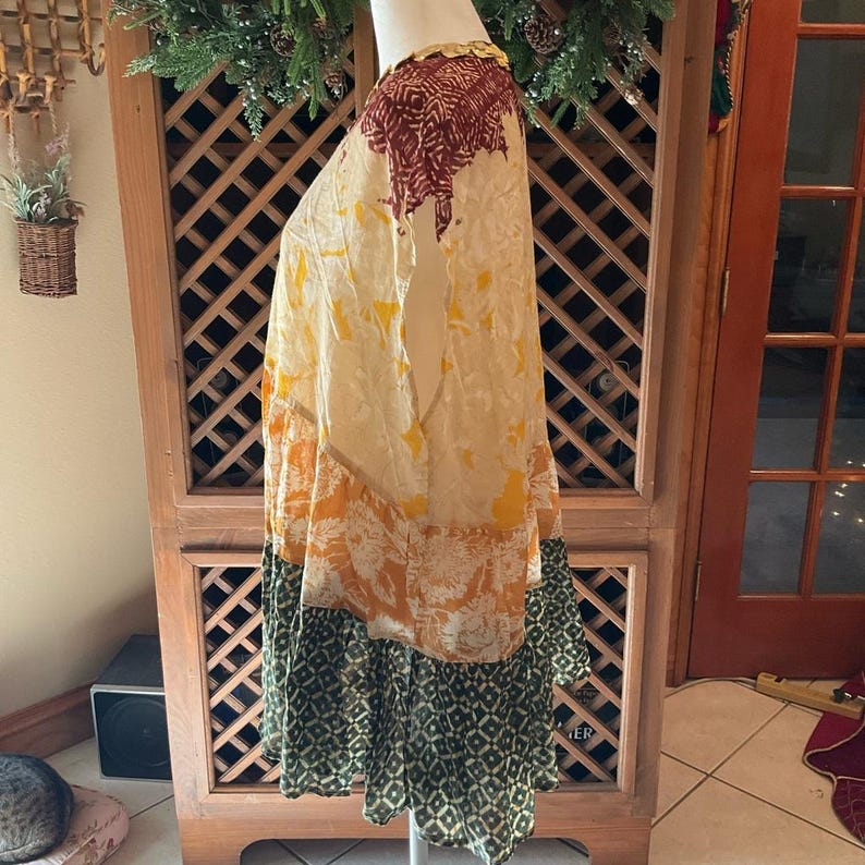 May include: A flowing, patterned dress in shades of cream, yellow, orange, and green. The dress features a tiered design with a ruffled hem and a mix of floral and geometric patterns. The top portion has a burgundy pattern.