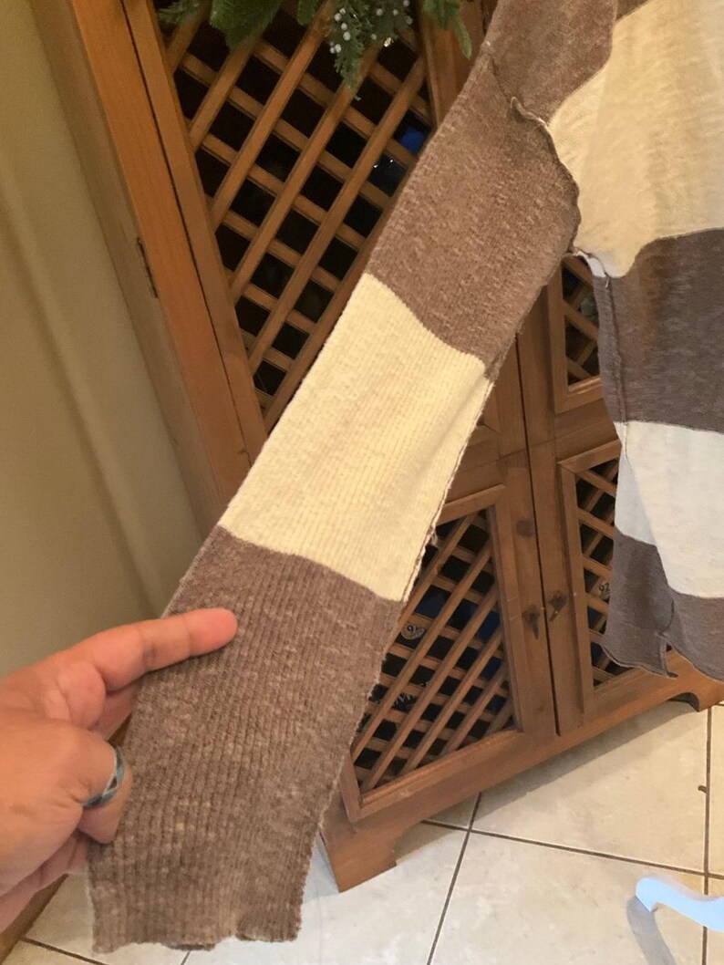May include: A long-sleeved sweater with a color block design. The sleeve features alternating sections of brown and cream colors. The sweater is made of a soft, textured material.