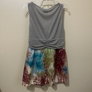 Pode incluir: Um vestido cinza sem mangas com uma saia de estampa floral. A saia tem um fundo branco com padr&otilde;es florais azuis, verdes e vermelhos.