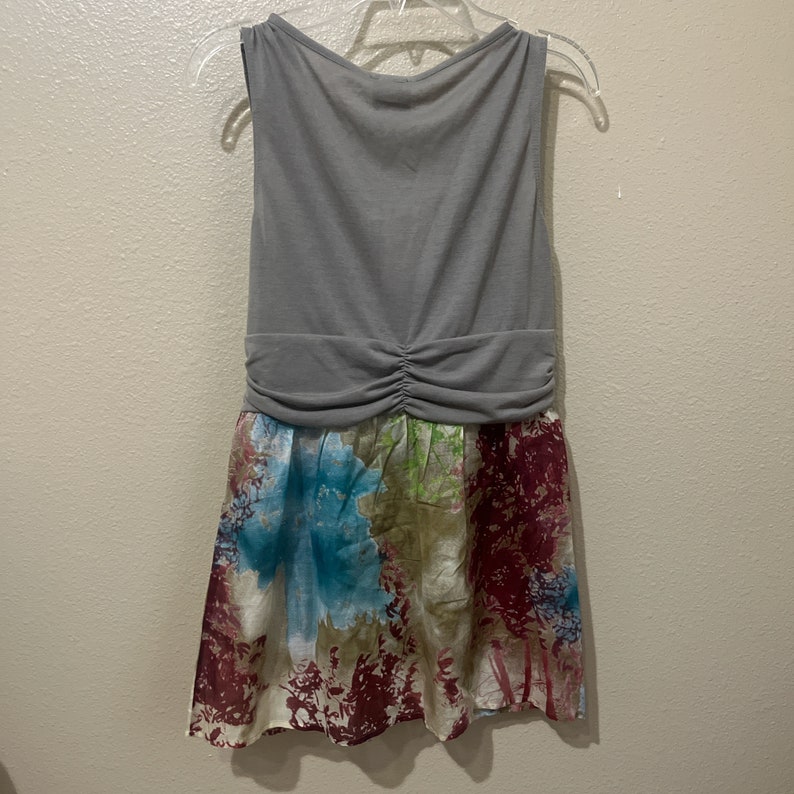 Pode incluir: Um vestido cinza sem mangas com uma saia de estampa floral. A saia tem um fundo branco com padr&otilde;es florais azuis, verdes e vermelhos.