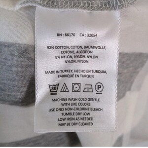 May include: A white fabric tag with black text and care symbols. The tag includes the RN and CA numbers, fabric composition, and washing instructions. The tag reads "Machine wash cold gentle with like colors."