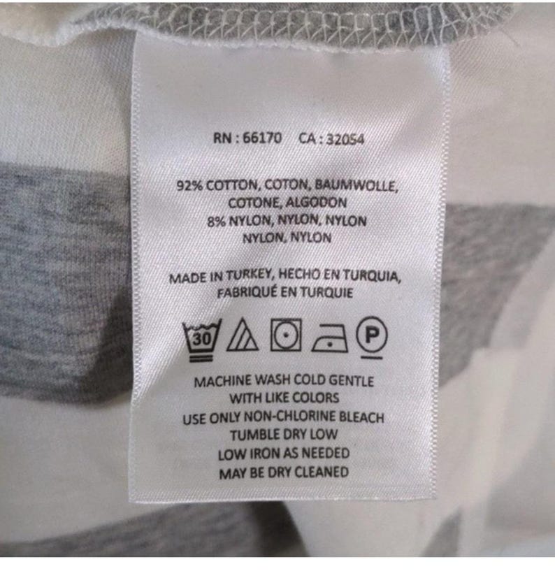 May include: A white fabric tag with black text and care symbols. The tag includes the RN and CA numbers, fabric composition, and washing instructions. The tag reads "Machine wash cold gentle with like colors."