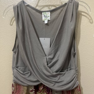 Pode incluir: Vestido cinza sem mangas com decote em V e design cruzado na frente. O vestido tem uma saia com estampa floral.