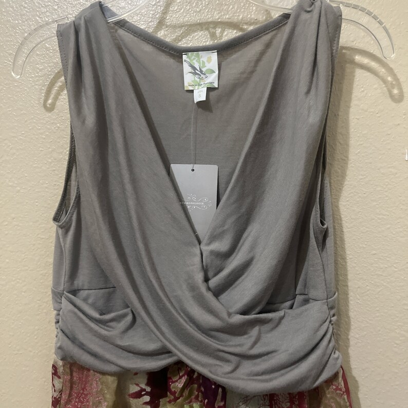 Pode incluir: Vestido cinza sem mangas com decote em V e design cruzado na frente. O vestido tem uma saia com estampa floral.