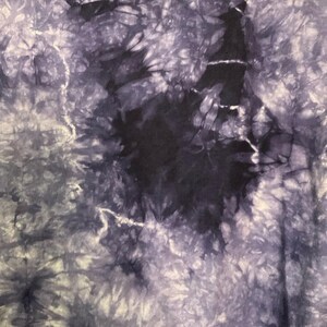 May include: A close-up view of a fabric with a tie-dye pattern. The fabric features a blend of dark blue, light blue, and white hues, creating a swirling, cloud-like effect. The design has a central dark blue area surrounded by lighter shades.