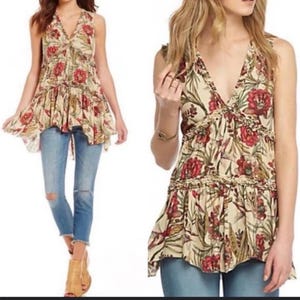 May include: A sleeveless top with a V-neck and a floral pattern in red, cream, and green. The top has a ruffled hem and is paired with blue jeans. The overall style is bohemian.