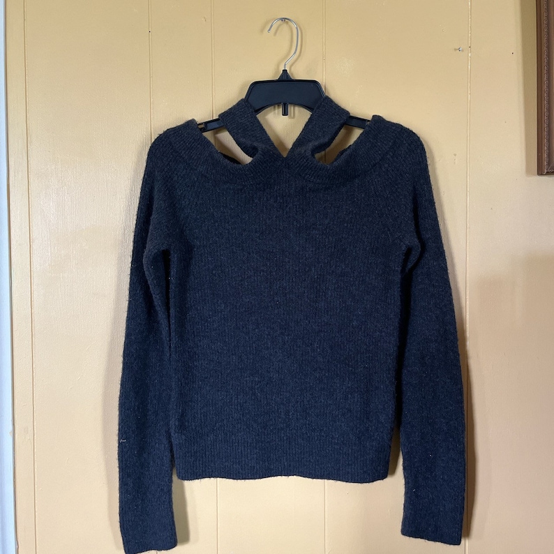May include: A dark gray sweater with long sleeves and a criss-cross detail at the neckline.
