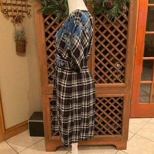 May include: A black and white plaid dress with blue floral embroidery on the shoulders and waist. The dress has a wrap-style bodice and a fitted waist. The dress is displayed on a mannequin.