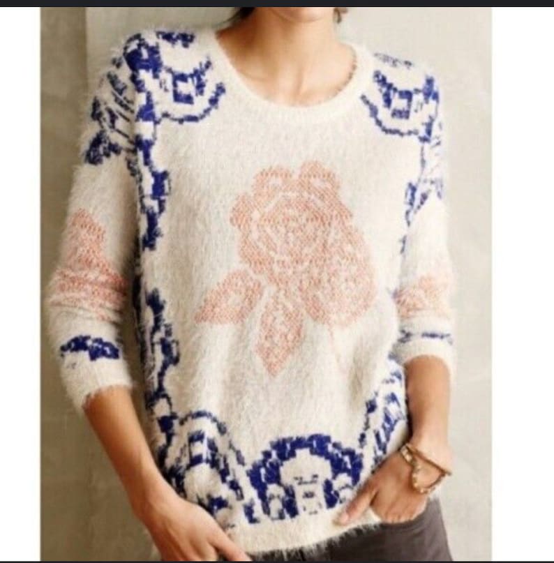 May include: A white fuzzy sweater with a pink rose design and blue and white geometric patterns around the edges.