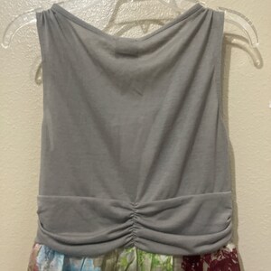 Pode incluir: Um vestido cinza sem mangas com cintura franzida. O vestido tem uma estampa floral na metade inferior.