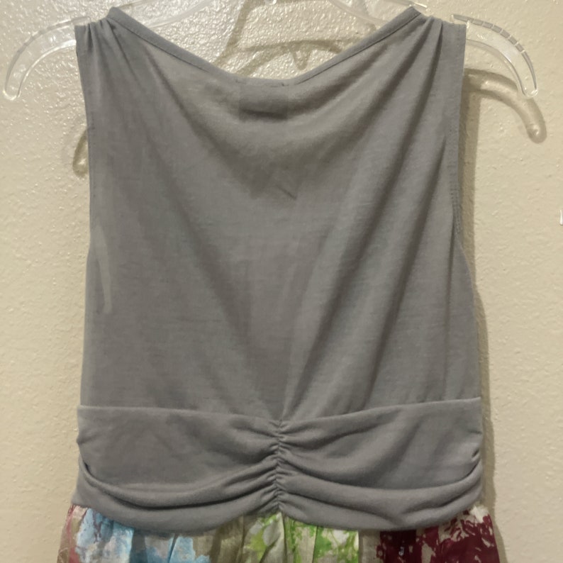 Pode incluir: Um vestido cinza sem mangas com cintura franzida. O vestido tem uma estampa floral na metade inferior.