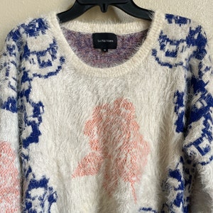 May include: White fuzzy sweater with a blue and white geometric pattern and a pink fuzzy tree design. The sweater has a crew neck and the brand label "La Free Verte" is visible on the front.