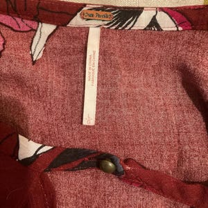 May include: Close-up of a burgundy-colored top with floral patterns in white, black, and pink. The tag reads "Free People" and "Made in China". The size is Large (L).