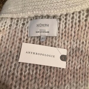 May include: Close-up of a textured, off-white and pink knit sweater. The label reads "N&Uuml;MPH MAKE AN ENTRANCE" and the tag says "ANTHROPOLOGIE". The sweater is a size L.