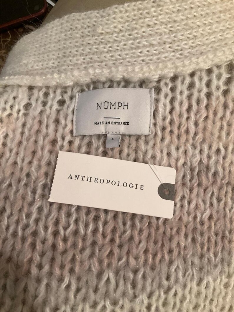 May include: Close-up of a textured, off-white and pink knit sweater. The label reads "N&Uuml;MPH MAKE AN ENTRANCE" and the tag says "ANTHROPOLOGIE". The sweater is a size L.