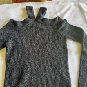 May include: A dark gray knitted sweater with a cut-out shoulder detail and a high neck.