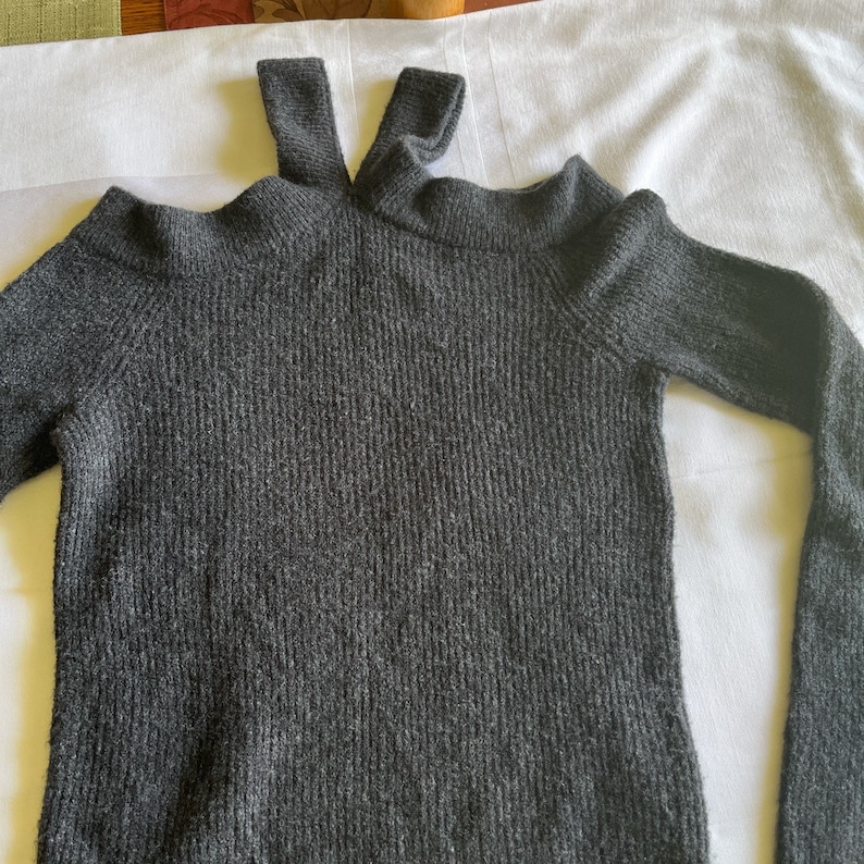 May include: A dark gray knitted sweater with a cut-out shoulder detail and a high neck.