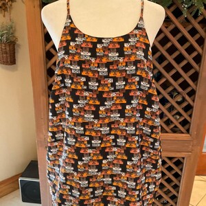 Puede incluir: Vestido camisola negro con un estampado repetido de maletas en tonos naranja, marr&oacute;n y gris. El vestido tiene finos tirantes espagueti y un escote redondo. La tela parece ligera.
