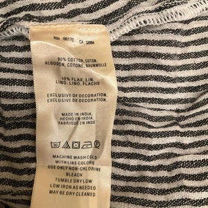 May include: A close-up of a clothing label with text. The label is cream-coloured with black text and includes washing instructions. The fabric is a black and white striped pattern. The label indicates the garment is made in India.
