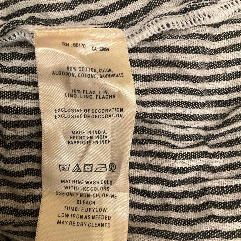 May include: A close-up of a clothing label with text. The label is cream-coloured with black text and includes washing instructions. The fabric is a black and white striped pattern. The label indicates the garment is made in India.