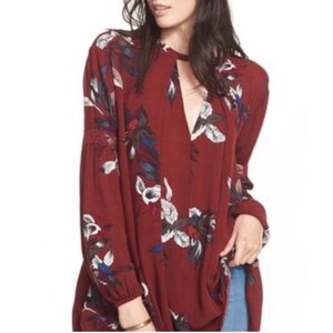 May include: A burgundy tunic top with a floral pattern. The long-sleeved top features a keyhole neckline and a relaxed fit. The floral design includes white, blue, and red accents, creating a bohemian style.