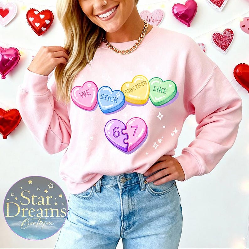 Pu&ograve; includere: Una felpa rosa chiaro con un design a forma di cuore di caramella. I cuori di caramella recitano "WE STICK TOGETHER LIKE" e "6 7". La felpa &egrave; a tema San Valentino.
