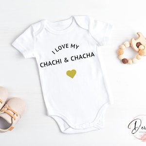 以下が含まれることがあります： 白いベビーロンパースに、黒い文字で「I love my Chachi & Chacha」と書いてあり、金色のハートが描かれています。