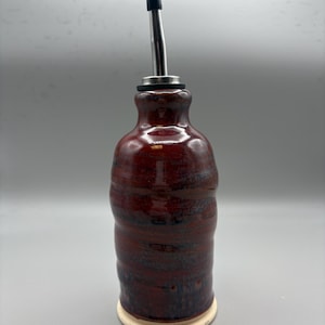 May include: A red ceramic oil and vinegar bottle with a stainless steel pour spout and a white base.