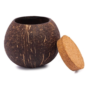 Può includere: Un contenitore in guscio di cocco marrone con un coperchio in sughero naturale. Il contenitore è realizzato con un guscio di cocco intero e ha un aspetto naturale e rustico.