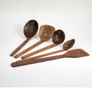 Peut inclure: Ensemble de cinq cuillères en bois fabriquées à partir de coques de noix de coco. Les cuillères sont de différentes tailles et formes, y compris une grande cuillère de service, une cuillère plus petite et une spatule plate.
