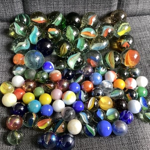 May include: A selection of glass marbles in a variety of colours and patterns. The marbles include shades of blue, green, orange, yellow, and white. Some have detailed designs, while others are plain. A traditional children's game.