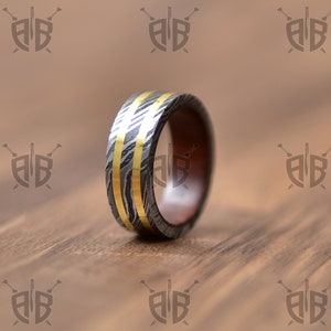 May include: A silver and gold ring with a wood inlay. The ring has a hammered finish and two gold bands.