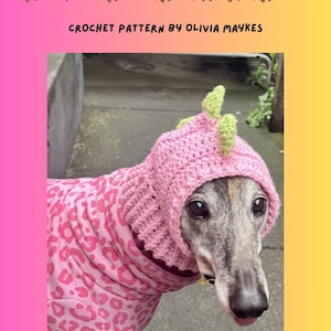 May include: A greyhound wearing a pink crocheted dinosaur snood with green spikes. The dog is also wearing a pink leopard print shirt. The image includes the text "GREYHOUND DINOSAUR SNOOD" and "CROCHET PATTERN BY OLIVIA MAYKES".