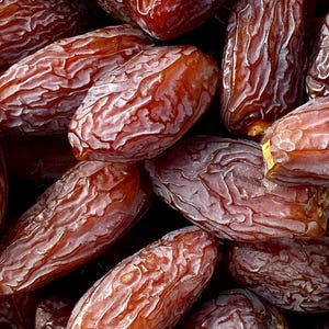 Op de afbeelding: Close-up van een stapel gedroogde dadels. De dadels zijn donkerbruin van kleur en hebben een gerimpelde textuur.