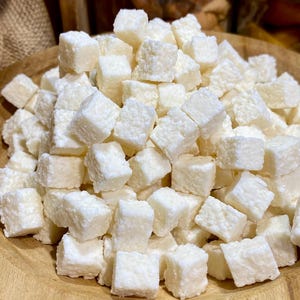 Peut inclure: Un bol en bois rempli de petits bonbons de noix de coco blancs en forme de cube.
