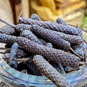 Peut inclure: Un bocal en verre rempli de grains de poivre longs séchés. Les grains de poivre sont brun foncé et ont une texture rugueuse.