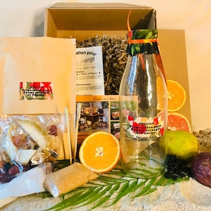 Peut inclure: Une bouteille en verre transparente avec un couvercle en tissu coloré et une étiquette indiquant "Préparation pour Rhums arrangés et Punchs". La bouteille est entourée de divers fruits, dont des oranges, des citrons verts et un fruit de la passion.