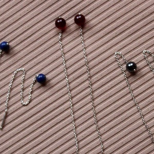 May include: Three pairs of dangle earrings with different colored beads. The first pair has blue beads, the second pair has red beads, and the third pair has black beads.