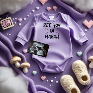 May include: A lilac baby onesie with the text "SEE YOU IN MARCH" is displayed with an ultrasound image, knitted slippers, and decorative hearts. The scene is set on a soft, purple blanket, with a small television prop.