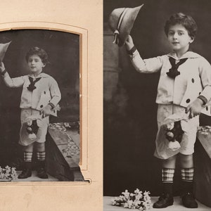 Puede incluir: Una fotograf&iacute;a en blanco y negro de un ni&ntilde;o peque&ntilde;o con un traje de marinero y sosteniendo un sombrero. Est&aacute; de pie frente a un fondo de flores.