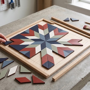 Puede incluir: Un marco cuadrado de madera que contiene un patrón de estrella geométrico hecho de piezas de madera pintadas e interconectadas en tonos azul marino, rojo apagado, verde salvia y crema. Piezas sueltas adicionales yacen cerca.