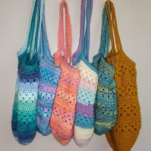 May include: A collection of six handmade crochet bags in various colors, including teal, orange, purple, and gold. Each bag has a long strap and a unique openwork or textured design, perfect for carrying items.